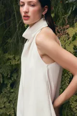 Top blanco satinado con cuello halter y escote fluido. Cierre en la espalda con botones.