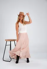 Pollera larga de color rosa pálido, con corte en capas y cintura elastizada. Incluye lazo fino del mismo material.