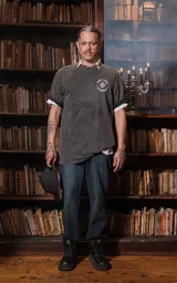 Remera negra con efecto nevado, de manga corta y cuello redondo, con calce oversize. Presenta una estampa en la espalda inspirada en el arcano "La Estrella" del Tarot, con una figura femenina vertiendo agua de dos cántaros, rodeada de estrellas y vegetación en colores vibrantes como amarillo, azul, rosa y verde.