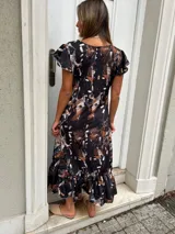 Vestido midi negro con estampado abstracto en tonos beige y blanco, mangas cortas con volados y falda con volados en el ruedo.