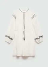 Vestido blanco de algodón con bordados negros en cuello, mangas y cintura. Tiene mangas 3/4 con puños elásticos, corte evasé y cintura elástica con lazo.