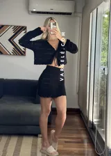 Conjunto de dos piezas tejido al crochet color crudo. Incluye una mini falda de tiro alto y un cardigan corto con mangas largas y lazos para atar en el frente.