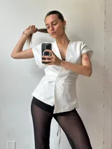 Chaleco blanco con finas rayas verticales celestes, escote en V, corte ajustado y cierre frontal con un botón.