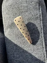 Broche triangular de acrílico color crema con lunares negros.