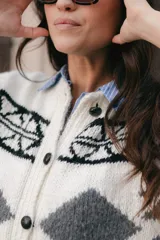 Chaleco de lana tejido a mano con diseño jacquard en negro, blanco y gris. Tiene cuello redondo y cierre frontal con botones de cuero.