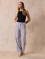 Pantalón de lino a rayas verticales en tonos beige, azul y blanco. Tiene pretina elastizada, bolsillos inclinados delanteros y bolsillo lateral tipo cargo.