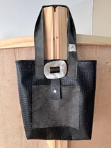 Bolso tote negro con textura símil cuero de cocodrilo, con bolsillo externo decorativo y cierre con botón metálico.