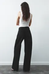Pantalón de jean celeste de tiro alto, corte wide leg y largo hasta el tobillo. Presenta un diseño asimétrico en la cintura con cierre frontal cruzado con cremallera y botones metálicos.