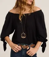 Blusa blanca de viscosa con escote off-shoulder y mangas 3/4 abullonadas con lazos en los puños.