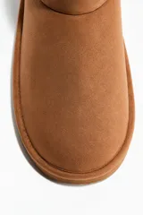 Botas cortas color tostado con forro interior suave y efecto peludito. Presentan costuras decorativas, una trabilla trasera y suela acanalada de 2 cm de grosor.