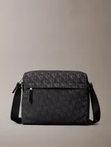 Bolso cruzado rectangular de color negro con estampado de monograma en tono gris oscuro. Cuenta con correa ajustable de tela negra y un tirador de cremallera de cuero negro.