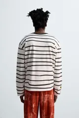 Camiseta relaxed fit de manga larga confeccionada en tejido compacto de algodón a rayas horizontales blancas y negras. Tiene cuello redondo y detalle de estampado de flores rojas en el bajo. Edición especial Zara x Otis Kwame Kye Quaicoe.