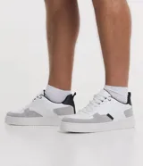 Championes urbanos de cuero sintético blanco con recortes en gris y negro, cierre con cordones y suela de goma.
