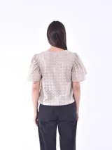 Blusa color blanco con mangas cortas abullonadas y calado con pequeños orificios.