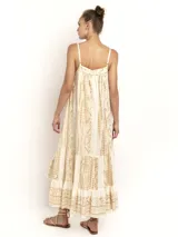 Vestido largo color crema con estampado dorado, de breteles finos y escote en V. Presenta una silueta amplia con caída fluida y detalle de volado en el ruedo.