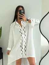 Vestido camisero blanco con aberturas geométricas en el frente, mangas largas con volados y bajo irregular.