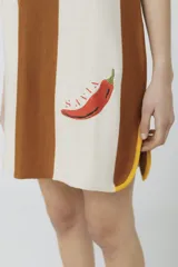 Vestido corto tejido en jersey liviano de algodón y acrílico, con diseño tipo polo y fit holgado. Presenta rayas verticales en color marrón y crudo, bordado XL de un ají y terminaciones en color amarillo.