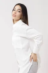 Camisa blanca de lino, de corte holgado, con cuello clásico, cierre frontal con botones, bolsillo en el pecho y mangas largas con puños abotonados.