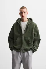 Sudadera negra relaxed fit de algodón compacto con interior en rizo, cuello con capucha ajustable, manga larga, bolsillos frontales tipo canguro, acabados en rib y cierre frontal con cremallera.