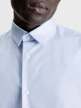 Camisa celeste de popelín de algodón superelástico, con cuello en punta, manga corta, tapeta con botones y logo con monograma de Calvin Klein en el pecho.