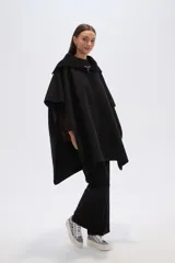Poncho negro de tejido grueso, con cuello alto de punto acanalado y cierre frontal con cremallera.