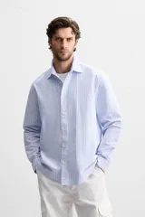 Camisa celeste con rayas verticales blancas, de corte regular, cuello solapa, manga larga con puños abotonados y cierre frontal con botones.