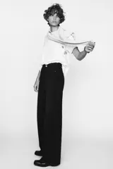 Pantalón de jean celeste de tiro alto, corte wide leg y largo hasta el tobillo. Presenta un diseño asimétrico en la cintura con cierre frontal cruzado con cremallera y botones metálicos.