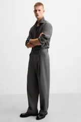 Pantalón negro de corte ancho con cinturón de tela con hebilla metálica y pliegues frontales.