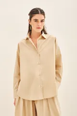 Camisa beige de poplin amplia, con botones laterales para abotonar de forma cruzada.