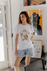 Remera blanca de algodón con calce relajado y estampa frontal de una flor grande con pétalos en tonos neutros y detalles en dorado.
