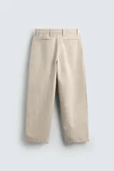 Pantalón chino color beige, de corte relaxed fit, confeccionado en tejido de mezcla de algodón y lino. Cuenta con bolsillos delanteros y traseros de vivo. Cierre frontal con cremallera y botón.