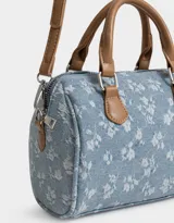 Cartera bowling de denim celeste con estampado de flores blancas, doble asa corta de cuero marrón y correa larga regulable y desmontable.