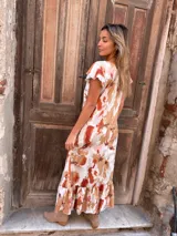 Vestido largo con estampado abstracto en tonos camel, naranja y blanco, con escote en V, mangas cortas con volados y falda con volados en el ruedo.