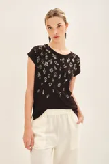 Remera negra de viscosa con calce suelto, escote redondo, manga corta y estampado frontal con bordado de lentejuelas doradas.