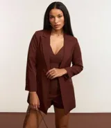 Blazer sastre femenino confeccionado en crepé color marrón, de modelo oversized y comprimento alargado. Sin estampa, posee bolsillos y detalle de pliegues en los puños.