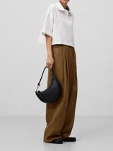 Bolso de hombro negro con textura granulada. Tiene un compartimento con cierre de cremallera, asa tubular con pieza metálica y logo grabado.