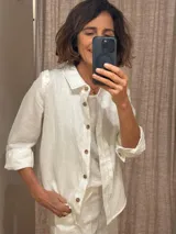 Camisa blanca de lino con corte femenino, cuello clásico, cierre frontal con botones de madera, mangas 3/4 con volados en los hombros y puños abotonados.