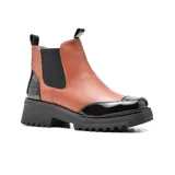 Bota Chelsea de cuero sintético negro con elástico lateral, puntera y talón charolados, plataforma track y tiradores en la caña.