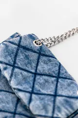 Bandolera azul de denim con diseño acolchado en forma de rombos. Tiene correa de cadena metálica y asa corta de denim.