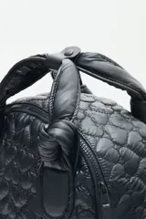 Mochila negra confeccionada en matelassé, con gran bolsillo frontal con cierre, bolsillos laterales y bolsillo interno porta notebook.