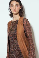 Chaleco largo color beige claro, estilo chaleco de gamuza, con apliques metálicos circulares perforados y largos flecos en el ruedo.