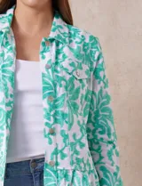 Campera blanca con bordado floral en verde agua, cuello solapa, cierre con botones, bolsillos delanteros y ruedo fruncido.