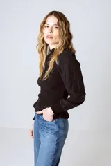 Blusa negra con cuello alto fruncido, mangas largas abullonadas y detalle de volado en el ruedo.