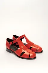 Sandalia roja de cuero vacuno con diseño de tiras entrecruzadas y hebilla lateral. Tiene suela de cuero artesanal y taco bajo.
