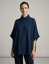 Capa o poncho tejido color verde esmeralda, con cuello polera alto que se cierra con un botón grande en el lateral. Presenta mangas cortas estilo japonesa y un calce amplio.