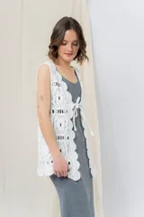 Chaleco tejido calado color crudo, con diseño artesanal, silueta relajada y largo a la cadera. Presenta terminación ondulada y detalle de lazo frontal.