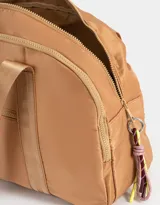 Bolso color beige de tela deportiva con manijas superiores y cierre superior. Tiene un bolsillo frontal con cierre y bolsillos laterales con cierre y tiradores de cordón y goma.