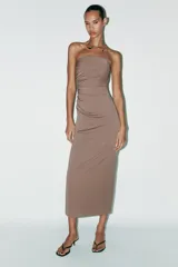 Vestido midi marrón de tejido de punto con escote recto y hombros descubiertos. Presenta detalle de collar metálico con aplicación de joyas, forro interior, bajo con abertura en la espalda, frunces en el tejido y cierre con cremallera oculta en la costura.