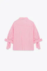 Camisa de lino a rayas verticales rosas y blancas, con cuello solapa, manga corta abullonada y lazos en los puños. Cierre frontal con botones ocultos.