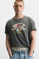 Camiseta gris de corte recto con cuello redondo y mangas cortas. Estampado ovalado con palmeras, sol y texto "Coconut Amora. Maui Offers Paradise".